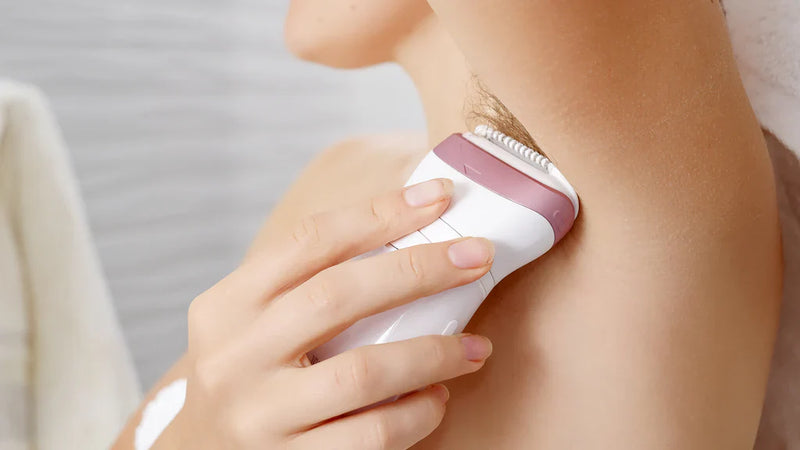 Woman using electric trimmer to remove underarm hair, personal care routine
